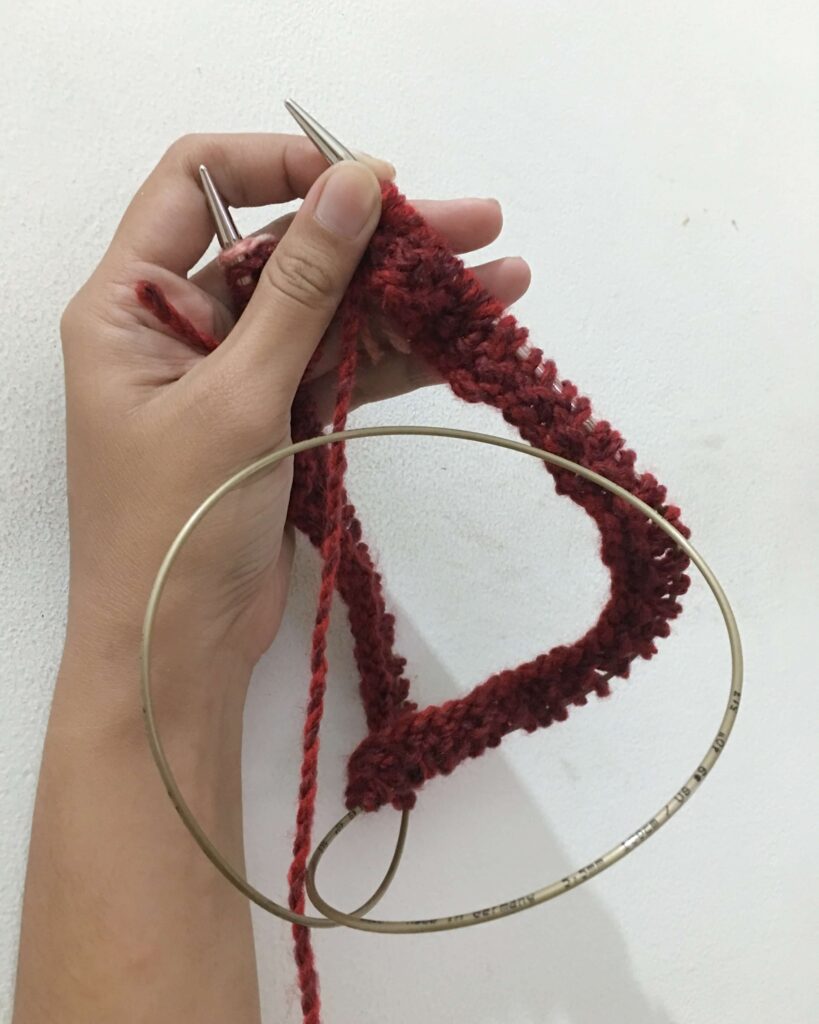 My hand holding knitted red yarn on circular needles